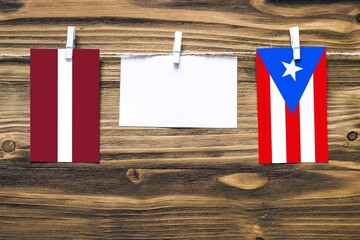 Hanging flags of Latvia and Puerto Rico attached to rope with clothes pins with copy space on white note paper on wooden background.Diplomatic relations between countries.