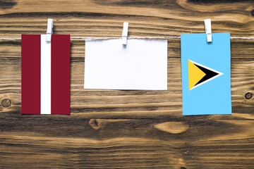 Hanging flags of Latvia and Saint Lucia attached to rope with clothes pins with copy space on white note paper on wooden background.Diplomatic relations between countries.