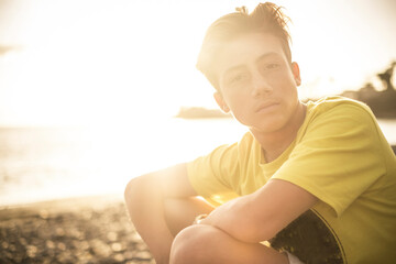 Beautiful portrait young handsome people male teenager looking at the camera sitting at the beach...
