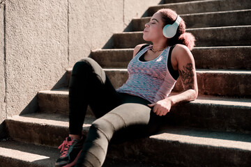 Charming young woman in headphones resting on stairs outdoors