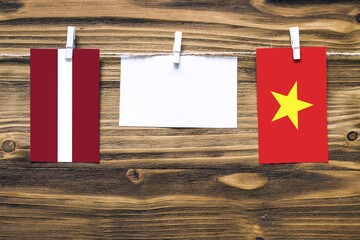 Hanging flags of Latvia and Vietnam attached to rope with clothes pins with copy space on white note paper on wooden background.Diplomatic relations between countries.