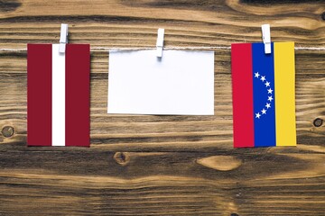 Hanging flags of Latvia and Venezuela attached to rope with clothes pins with copy space on white note paper on wooden background.Diplomatic relations between countries.