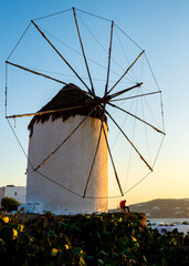 A young male in red shirt enjoying sunset next to windmill in Mykonos