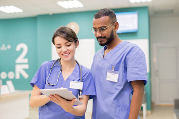 Two young successful clinicians in uniform looking through online medical new