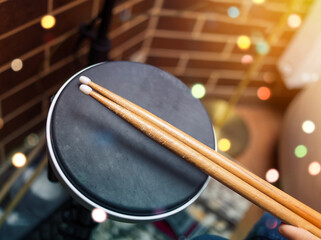 blurry image of drum and wooden drumsticks in hands. Girl learning and play drum set in music room,...