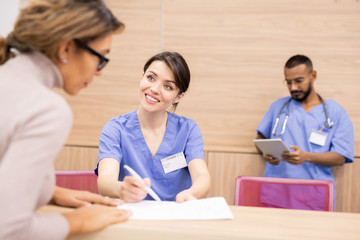Clinician in uniform smiling at patient while pointing at medical document
