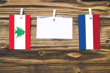 Hanging flags of Lebanon and Netherlands attached to rope with clothes pins with copy space on white note paper on wooden background.Diplomatic relations between countries.