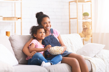Two happy african girls watching comedy movie on tv