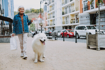 Elderly Caucasian lady walking with dog in street
