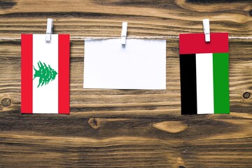 Hanging flags of Lebanon and United Arab Emirates attached to rope with clothes pins with copy space on white note paper on wooden background.Diplomatic relations between countries.