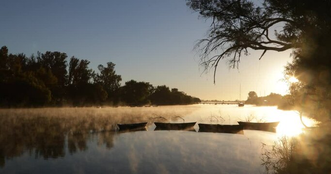 Golden foggy morning on river, movement of mist over water surface, silhouette of old rowing boats. Volume light and flares. Mysterious, calm scene. Rio Negro, Mercedes, Uruguay