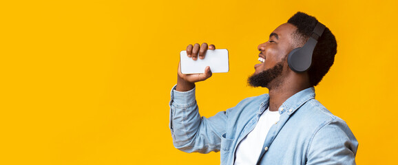 Carefree black guy holding smartphone and singing into it