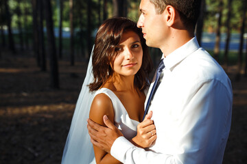 Obraz premium A happy newlywed couple of the bride and groom are walking on nature in a green forest. The bride and groom hug and kiss.Together. Young family. Marriage. Wedding concept.