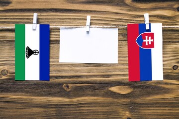 Hanging flags of Lesotho and Slovakia attached to rope with clothes pins with copy space on white...