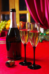 Two glasses of champagne and a bottle on the festive table with a red tablecloth