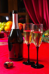 Two glasses of champagne and a bottle on the festive table with a red tablecloth