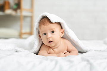 Fototapeta na wymiar Cute newborn boy peeking out under soft white blanket