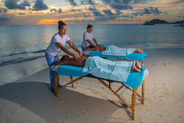 Women giving massage therapy stretch head neck outdoor at Caribbean beach to a couple on the massage table portable to relax. Caribbean turquoise water and sunset beach background . - Powered by Adobe