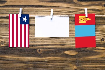 Hanging flags of Liberia and Mongolia attached to rope with clothes pins with copy space on white note paper on wooden background.Diplomatic relations between countries.