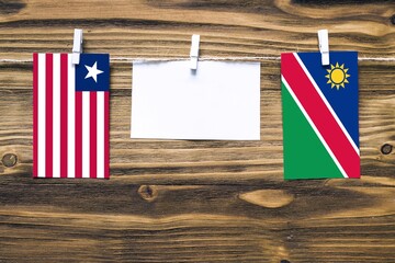 Hanging flags of Liberia and Namibia attached to rope with clothes pins with copy space on white note paper on wooden background.Diplomatic relations between countries.