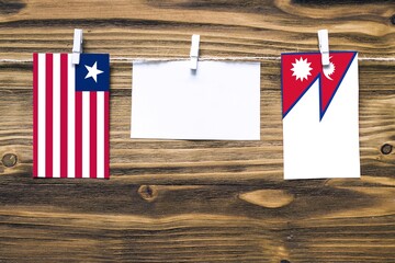 Hanging flags of Liberia and Nepal attached to rope with clothes pins with copy space on white note paper on wooden background.Diplomatic relations between countries.