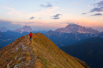 A hiker admires the sunset on Pelmo and Civetta seen from the summit of Migogn Mount, Dolomites, Marmolada group, Rocca Pietore, Belluno province, Veneto, Italy.
