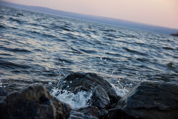 Sea wave beats on the rock against the sunset