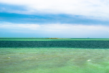 breathtaking beach view of the greenish water of the open sea and white clouds and clue sky in the background