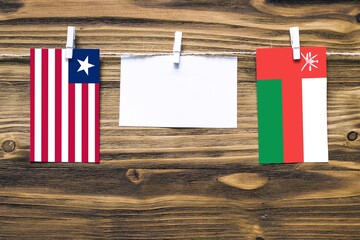 Hanging flags of Liberia and Oman attached to rope with clothes pins with copy space on white note paper on wooden background.Diplomatic relations between countries.