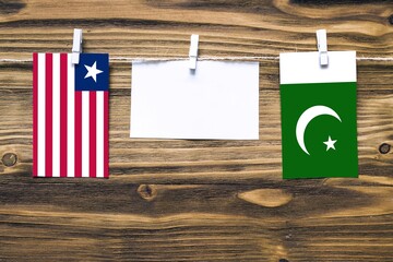 Hanging flags of Liberia and Pakistan attached to rope with clothes pins with copy space on white note paper on wooden background.Diplomatic relations between countries.