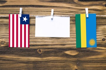 Hanging flags of Liberia and Rwanda attached to rope with clothes pins with copy space on white note paper on wooden background.Diplomatic relations between countries.