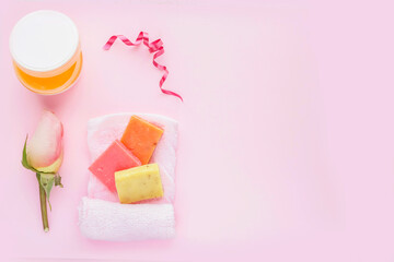 Open jar of cosmetic cream, soap, rose and towel on pink background. Concept of natural spa cosmetics. Flat lay, top view, copy space .	