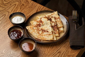 Homemade pancakes with jam, honey and sour cream bowls, close-up