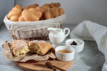 Delicious breakfast concept, close-up. A broken croissant with cream lies on a wooden board, with a honey bowl and a jug of cream.