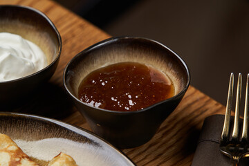 Homemade pancakes with jam, honey and sour cream bowls, close-up