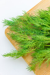 Bunch of the fresh dill leaves on a wooden cutting board close-up isolated on a white background