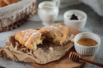 delicious breakfast composition, close-up. A broken croissant with cream lies on a wooden board, with a honey bowl and a jug of cream.