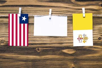 Hanging flags of Liberia and Vatican City attached to rope with clothes pins with copy space on white note paper on wooden background.Diplomatic relations between countries.