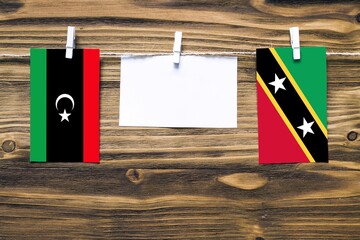 Hanging flags of Libya and Saint Kitts And Nevis attached to rope with clothes pins with copy space on white note paper on wooden background.Diplomatic relations between countries.