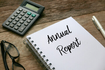 Top view of sunglasses,calculator,pen, and notebook written with Annual Report on wooden background.