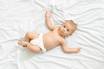 Portrait of curious newborn baby in diaper lying on bed