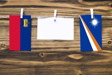 Hanging flags of Liechtenstein and Marshall Islands attached to rope with clothes pins with copy...