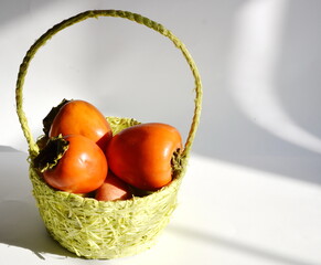 On the table is a basket of delicious orange persimmon fruit.