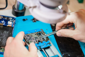 Tweezers in hands of repairman using microscope during work with tiny details