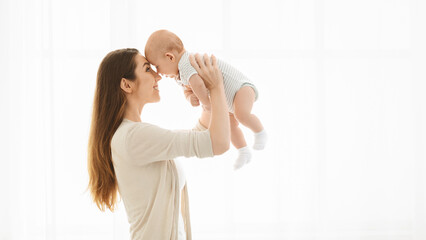 Mother lifting her baby up against window at home