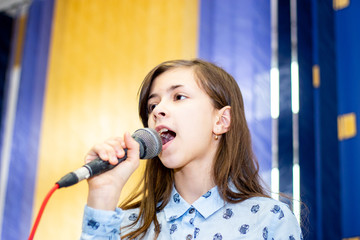 Teen girl learning to sing at a music school. Scene and microphone.