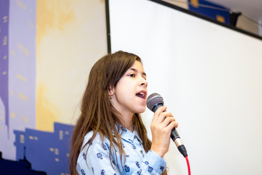Teen girl learning to sing at a music school. Scene and microphone.