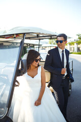 Luxury elegant wedding couple kissing and embracing near the car for golf. A stylish bridegroom in a black suit gently embraces a beautiful bride in a white dress. Together. Young family. Marriage.