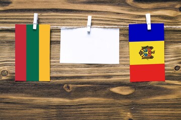 Hanging flags of Lithuania and Moldova attached to rope with clothes pins with copy space on white note paper on wooden background.Diplomatic relations between countries.