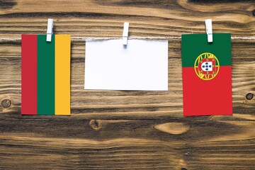 Hanging flags of Lithuania and Portugal attached to rope with clothes pins with copy space on white note paper on wooden background.Diplomatic relations between countries.